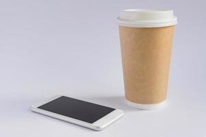 xícara de café de papel artesanal e smartphone metálico em fundo cinza em estilo minimalista foto