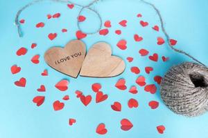 conceito de dia dos namorados e feriados - dois corações de madeira, recortar pequenos corações de papel no fundo azul. decoração artesanal. foto