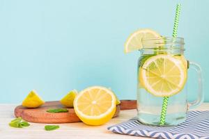 água de limonada cítrica com limão fatiado e hortelã, bebida de água saudável e desintoxicante no verão na mesa de madeira com fundo azul claro foto