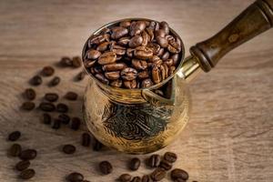 close-up de grãos de café torrados frescos em bule de café turco tradicional cezve na mesa de madeira. foto