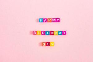 feliz aniversário filho inscrição feita de grânulos de cubo colorido com letras. conceito de fundo rosa festivo com espaço de cópia foto
