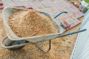 colocação de blocos de pavimentação de concreto vermelho e cinza. pavimentação de estradas, construção. carrinho de mão cheio de areia foto