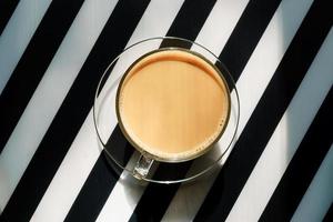 xícara de café quente com leite em um fundo listrado preto e branco. espaço de cópia foto