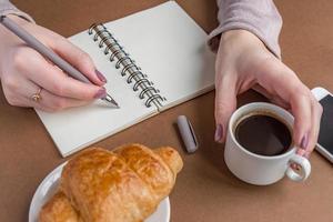 mulher com manicure escrevendo no notebook. freelancer trabalhando ao ar livre. coffee break com croissant foto