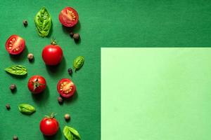 tomates cereja suculentos cortados ao meio e folhas de manjericão em um fundo verde. conceito de nutrição saudável. vista do topo. copie o espaço. foto