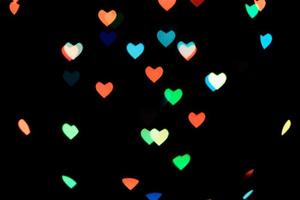 bokeh de corações multicoloridos de cores azuis e laranja sobre fundo preto. textura para férias foto