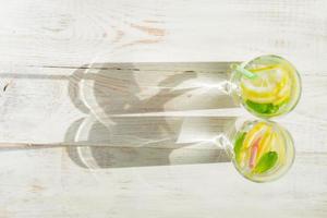 copo de limonada caseira com limões, hortelã e canudos de papel em fundo rústico de madeira. bebida refrescante de verão. sombras duras foto