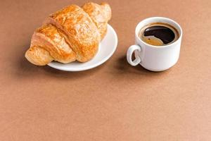 saboroso café da manhã. croissant francês servido na chapa branca e xícara de café preto ou expresso em fundo marrom. copie o espaço. foto