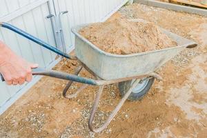 trabalhador no canteiro de obras segurando o carrinho de mão com areia. foto