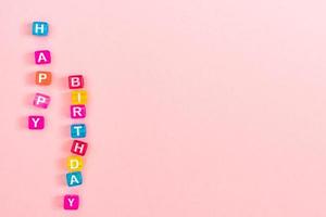 inscrição de feliz aniversário feita de grânulos de cubo colorido com letras. conceito de fundo rosa festivo com espaço de cópia foto