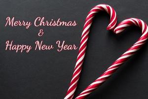 feliz natal e feliz ano novo cartão. coração feito de bastões de doces em fundo preto foto