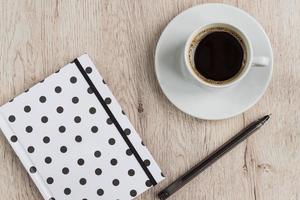 conceito de negócios e escritório - caderno de capa de bolinhas preto e branco, caneta e xícara de café preto na mesa de madeira. vista do topo. foto