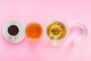 vista superior de diferentes bebidas - bebendo café, água com gás, suco de maçã e chá verde em fundo rosa. conceito de vida e dieta saudável foto