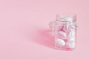 merengues torcidos brancos e rosa em uma jarra de vidro no fundo rosa. sobremesa francesa preparada com chantilly com açúcar e claras de ovos assadas. cartão com espaço de cópia foto