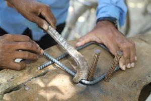 trabalhador dobrar haste de aço usando dobrador em um canteiro de obras. closeup tiro de mão masculina com vergalhões de metal dobrando dobrador com trabalho manual. o trabalhador está com as mãos nuas, o que não é seguro para este trabalho foto