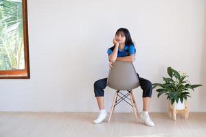 a garota sentada na cadeira cinza com planta verde no quarto mínimo. foto