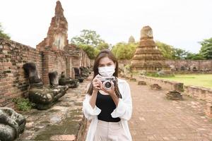 jovem mulher bonita usando máscara protetora viajando e tirando fotos no parque histórico tailandês, feriados e conceito de turismo cultural.