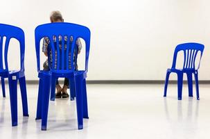 uma vista por trás de uma cadeira de plástico azul que está distante de um único homem idoso. foto