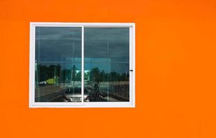 o fundo laranja da parede de concreto do prédio e as janelas brancas com vidro transparente refletem. foto