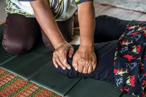 close-up vista de ambas as mãos de uma massagista tailandesa idosa apertando e dobrando as pernas. foto