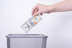 uma mão joga notas de dólar em uma lata de lixo contra um fundo cinza. foto