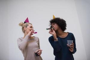 mulheres sorridentes em bonés de festa soprando apitos foto