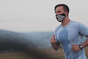 homem fitness em roupas esportivas molhadas usando máscara facial protetora preta correndo ao ar livre na cidade durante o surto de coronavírus. covid 19 e atividade física de jogging esporte e fitness. novo normal foto