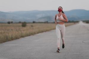 determinada mulher fitness em roupas curtas usando máscara facial protetora vermelha correndo ao ar livre na cidade durante o surto de coronavírus. covid 19 e atividade física de jogging esporte e fitness. foto