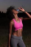 mulher afro-americana bebendo água depois de correr na natureza foto