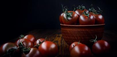 tomates suculentos maduros em um prato de barro e ao lado dele em um fundo preto. foto