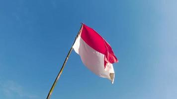 bandeira indonésia com uma vara de bambu acenando alto no céu. dia da independência da indonésia 17 de agosto foto