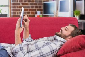 homem casual usando tablet digital no sofá foto