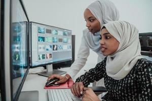 amigos no escritório duas jovens empresárias muçulmanas modernas afro-americanas usando cachecol no local de trabalho de escritório brilhante criativo com uma tela grande foto