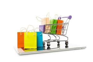 saco de compras em um carrinho com tablet em fundo branco, compras on-line ou conceito de comércio eletrônico foto