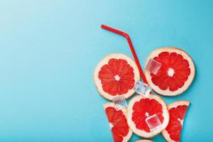 uma composição de fatias de toranja e cubos de gelo com um canudo em um fundo azul na forma de uma bebida refrescante. foto