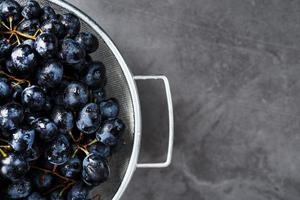 uvas pretas doces em uma tigela de metal em um plano de fundo texturizado escuro. foto