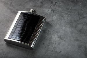 frasco de aço em acabamento de couro para álcool em um fundo escuro com espaço de cópia foto