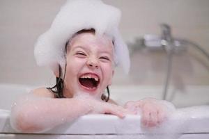 menina no banho brincando com espuma de sabão foto