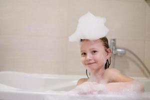 menina no banho brincando com espuma de sabão foto