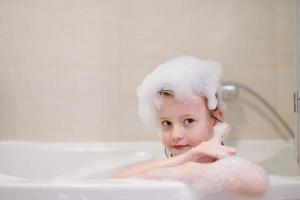 menina no banho brincando com espuma de sabão foto