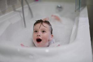 menina no banho brincando com espuma de sabão foto