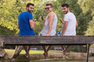 homens desfrutando de melancia enquanto está sentado na ponte de madeira foto