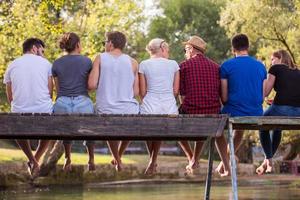 vista traseira de amigos desfrutando de melancia enquanto está sentado na ponte de madeira foto