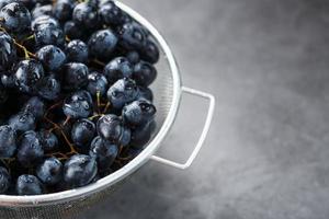 uvas pretas doces em uma tigela de metal em um plano de fundo texturizado escuro. foto