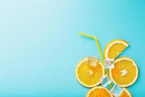 uma composição de fatias de laranja e cubos de gelo com um canudo em um fundo azul na forma de uma bebida refrescante foto