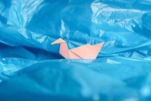 origami de pássaro de papel rosa entre um saco plástico azul como se estivesse em ondas de água ou céu azul. foto conceitual