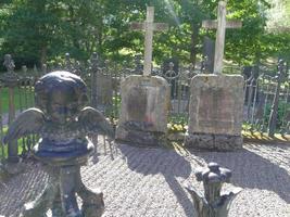 estátua de anjo misteriosa com asas na frente de duas sepulturas com pedras e cruzes no cemitério assustador foto