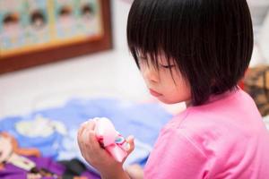 criança asiática fez uma cara triste, olhando para o grampo de cabelo danificado em sua mão. uma menina de 4 anos vestindo uma camisa rosa. foto