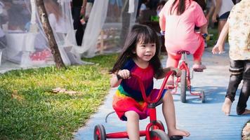 garota se divertiu andando de triciclo vermelho. crianças fofas sorriem e riem se divertem. criança feliz está vestida de cores brilhantes, com 4 anos de idade. foto