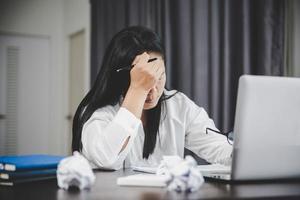 estresse mulher de negócios do trabalho duro, depressão no escritório. trabalhadora cansada e ansiosa com infeliz no trabalho problemático. jovem empresária sentada triste frente do computador portátil na mesa. foto